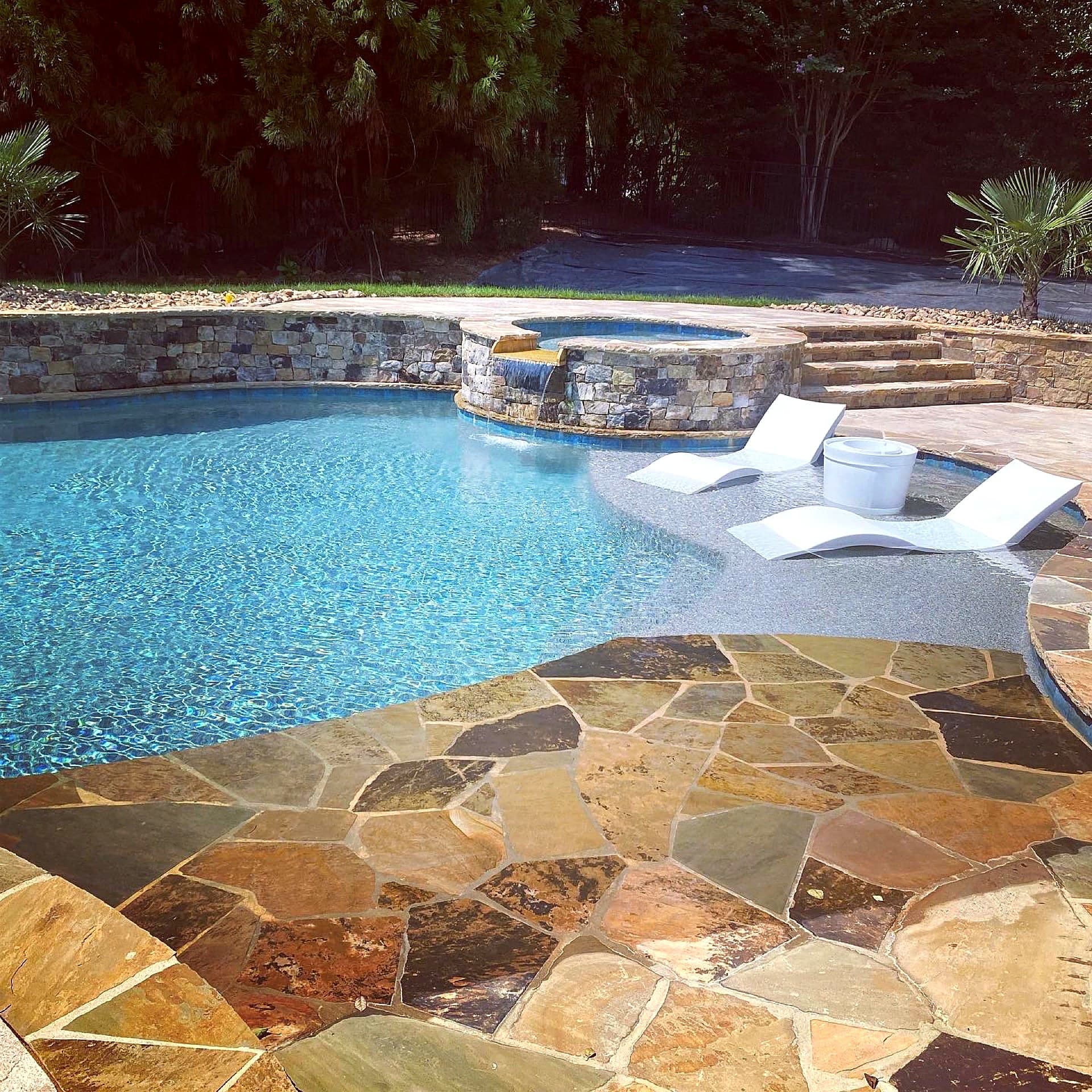 Freeform pool with raised spa and waterfall surrounded by natural stone in Charlotte NC