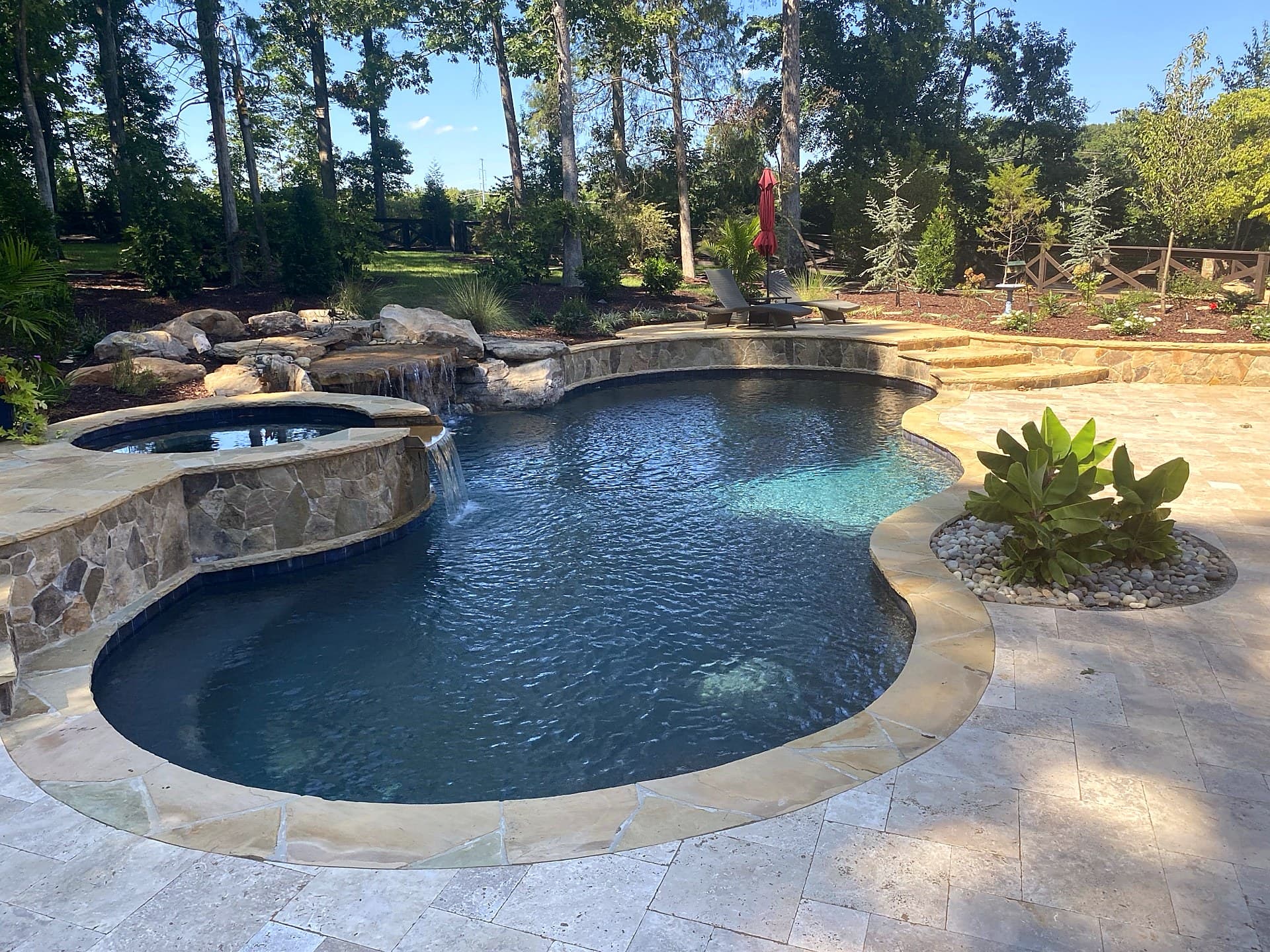 Tropical pool oasis with rock waterfall by Blue Waters Construction